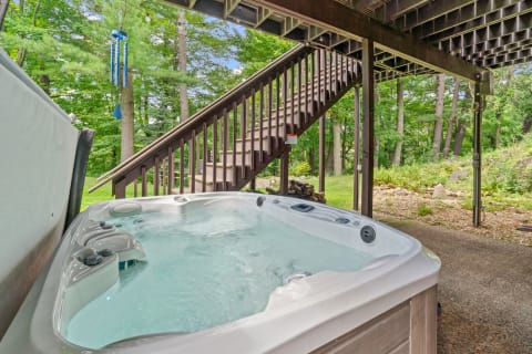 Hot tub on a patio with wooden stairs and green trees in the background.