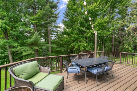Outdoor deck with green couch, dining table and string lights surrounded by trees.