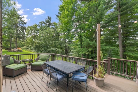 Outdoor deck with dining table, chairs, and green cushions surrounded by trees.
