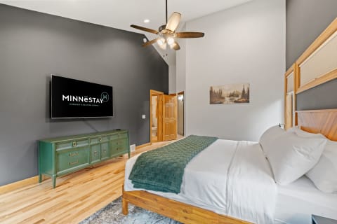 A cozy and modern bedroom featuring a green dresser, flat-screen TV, and a serene painting of nature.