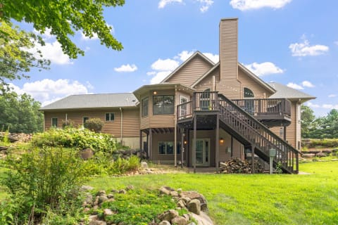 A modern house with a brown exterior and large windows surrounded by a green lawn and trees.