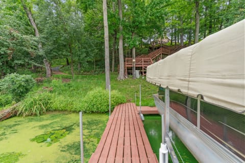A dock extending over green water with a covered boat, surrounded by trees and paths.