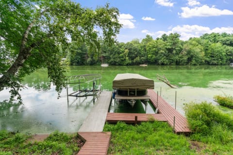 Lakeside scene with a dock and covered boat surrounded by trees and a green water surface.
