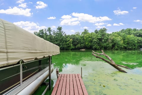 Lakeside scene with a wooden dock, a covered boat, and green water.