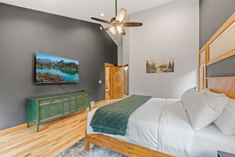Modern bedroom with a comfortable bed, green throw blanket, and a mounted television displaying a scenic landscape.
