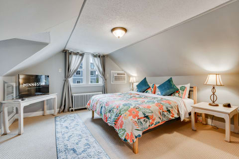 Cozy bedroom featuring a floral duvet, nightstands with lamps, and a television, set under an angled ceiling.
