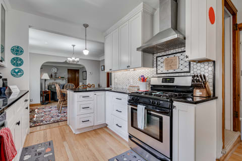 Modern kitchen with white cabinets, dark countertops, stainless steel stove, and hexagonal tile backsplash.