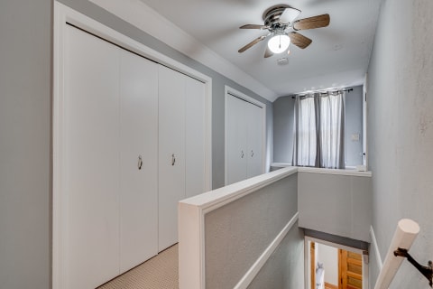 An upper hallway featuring gray walls, white sliding doors, and a ceiling fan.