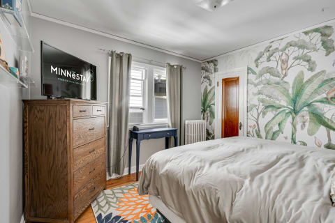 A stylish bedroom featuring a tropical mural, dresser, television, and modern decor.
