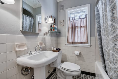 A compact bathroom with a vintage sink, a modern toilet, and a patterned shower curtain.