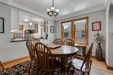 Dining room with round wooden table, surrounded by chairs, and a view into a modern kitchen.