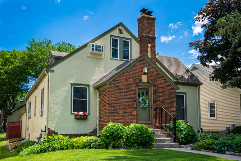 Residential house featuring brick and stucco design, green landscaping, and a blue sky.