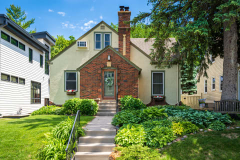 A suburban house with brick and stucco exterior, surrounded by lush greenery and flower boxes.