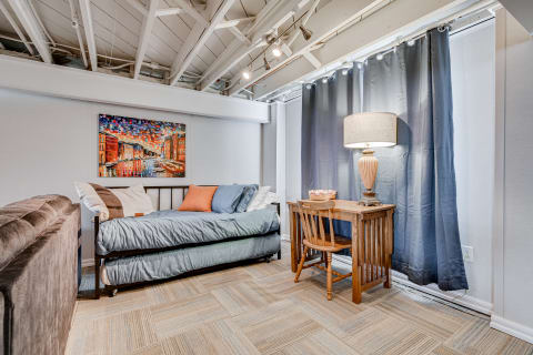 Interior of a cozy room with a daybed, desk, and colorful artwork on the wall.