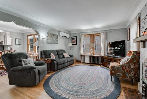 A cozy living room featuring gray sofas, a colorful rug, and a television, illuminated by natural light.