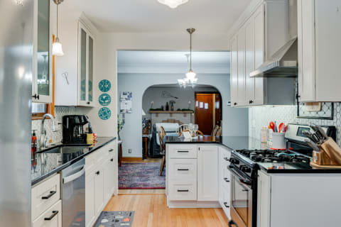 A modern kitchen with white cabinets, black countertops, and a cozy dining area visible in the background.