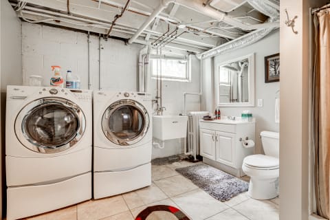 Interior view of a laundry and bathroom with white appliances and fixtures, including a sink and toilet.