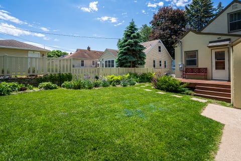 A serene backyard featuring a green lawn, flower beds, and a charming house with a deck.