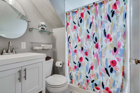 A modern bathroom with a white vanity, floral shower curtain, and organized towel rack.