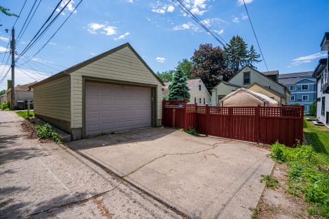 A light-colored garage next to a red fence in a residential alley.