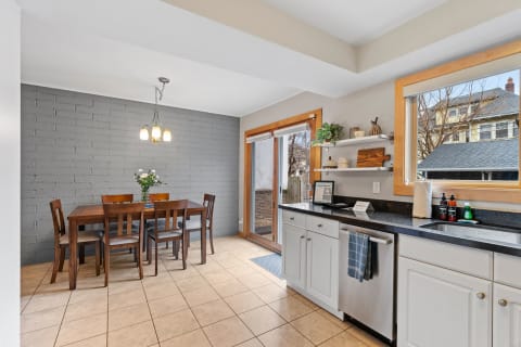 A kitchen featuring a wooden dining table, gray brick wall, and bright natural light from the windows.