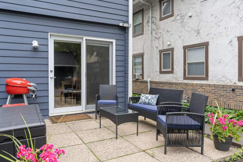 An outdoor patio with wicker furniture, a red grill, and pink flowers.