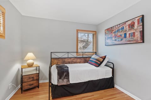 A well-lit bedroom featuring a single bed with colorful pillows and a wooden nightstand.
