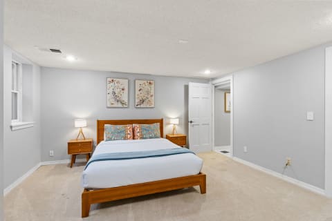 A neatly arranged bedroom with a wooden bed, colorful pillows, and framed floral artwork.
