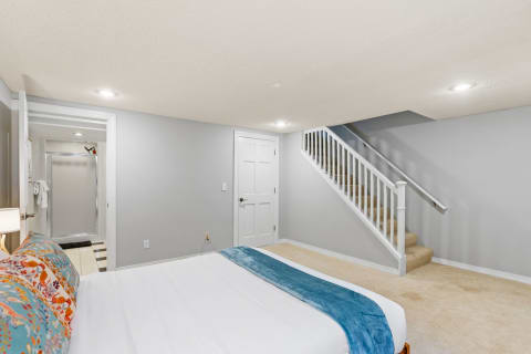 A cozy basement bedroom featuring a bed, staircase, and bathroom access.