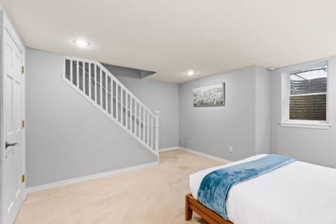 A bright and inviting basement bedroom featuring a bed, staircase, and artwork on the wall.