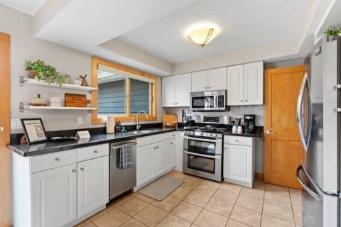 Modern kitchen featuring white cabinets, granite countertops, and open shelving with decorative items.
