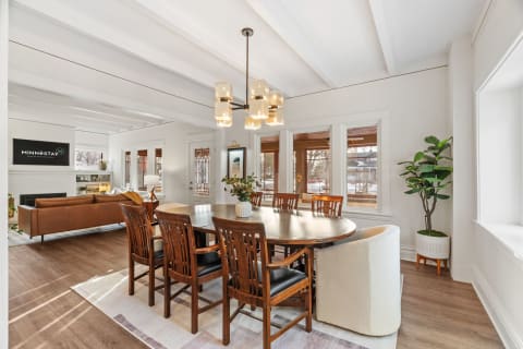 A bright dining area with a wooden table and elegant pendant lighting, complemented by a leather sofa and greenery.