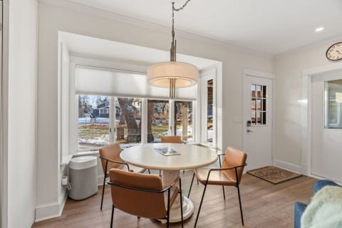 Stylish dining area with a round table, modern chairs, and bay windows overlooking a garden.