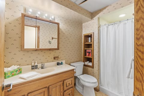 Cozy bathroom with a wood vanity, vintage wallpaper, and a shower curtain.