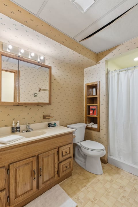 A compact bathroom with wooden vanity, toiletries, and a walk-in shower.