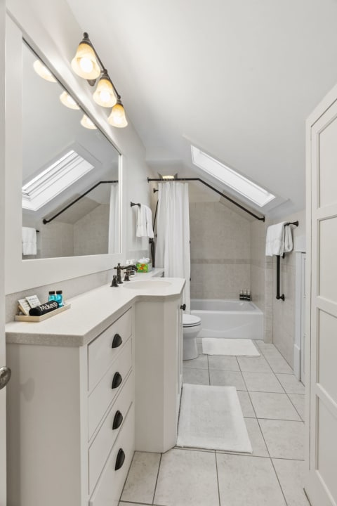 A bright attic bathroom with skylights, an elegant vanity, and a cozy bathtub.