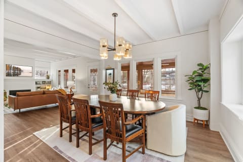 Spacious dining area with a round table, wooden chairs, and exposed beams overhead.