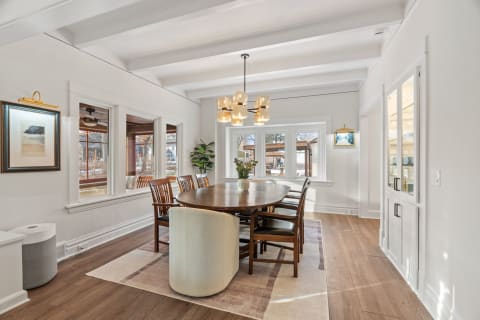 A bright dining room with a wooden table, stylish chairs, and beautiful windows overlooking the outdoors.
