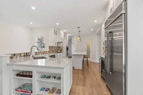 A sleek and modern kitchen featuring white cabinetry, wooden flooring, and a variety of board games on display.