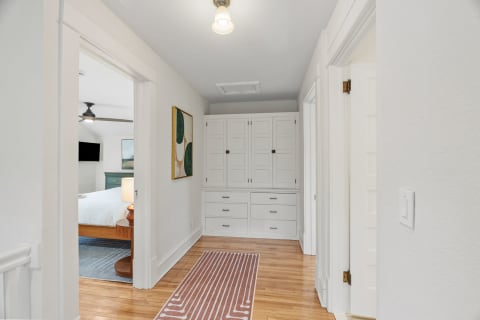 A hallway with hardwood floors, built-in white storage, and decorative artwork on the wall.