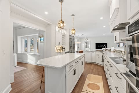 Modern gourmet kitchen with white cabinetry, marble countertops, pendant lights, and wooden flooring.