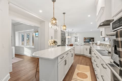 Modern kitchen featuring marble countertops, white cabinetry, and stylish pendant lights.