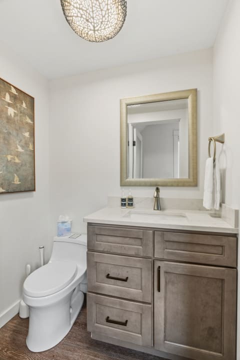 A modern powder room featuring marble countertops, a stylish mirror, and an artistic wall decor.