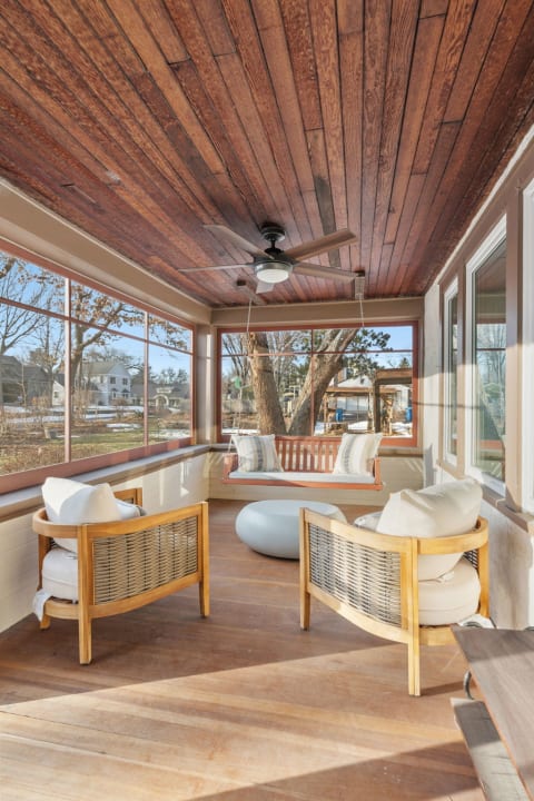 A bright and cozy screened porch featuring wooden ceilings, modern furnishings, and large windows overlooking a backyard.