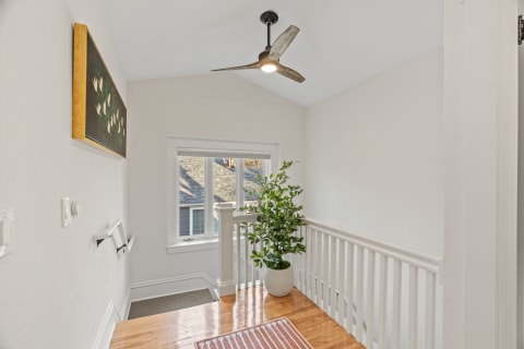A stylish upstairs landing with hardwood floors, ceiling fan, and a decorative indoor plant.