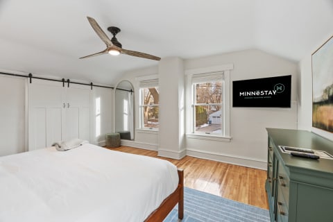 A bright bedroom featuring a king-size bed, sliding barn doors, large windows, and a mounted TV.