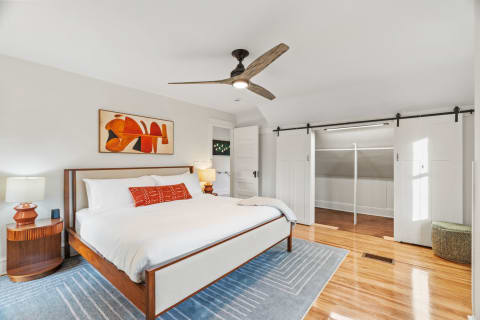 Stylish modern bedroom with wooden flooring, a bed with white linens, and contemporary artwork on the wall.