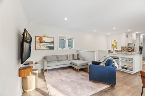 Bright and modern living room with grey sectional, blue armchair, and open kitchen in the background.