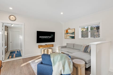 A modern living room with a large grey sofa, wall-mounted TV, and decorative artwork, bathed in natural light.