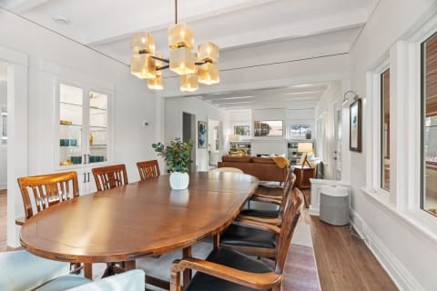 Elegant dining space with a wooden table and a glass chandelier, leading into a cozy living room.